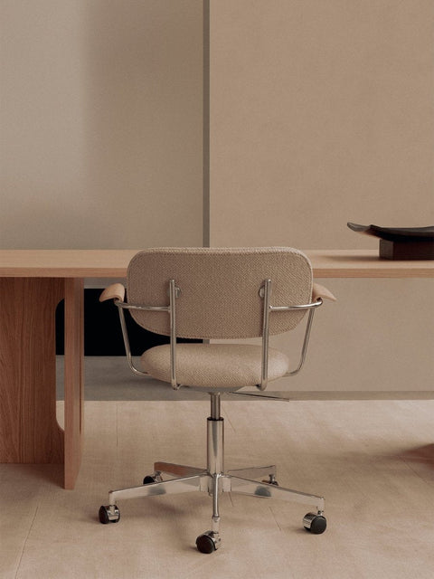 Audo Copenhagen Co Task Chair, Fully Upholstered, Without Arms, back view of the beige Co Task Chair with a chrome base at a light oak Androgyne Dining Table with a dark Releve Platter