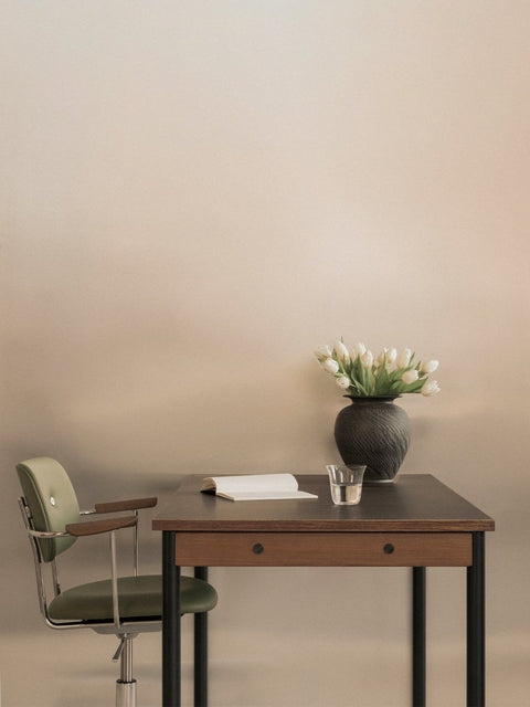 Audo Copenhagen Co Task Chair, Fully Upholstered, Without Arms, Co Task Chair, Fully Upholstered in green, at a wood desk with a book, a glass of water, and a vase of white tulips