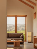Audo Copenhagen Conrad Lounge Table, natural oak Conrad Lounge Table and Offset Sofa in a bright room with a Hashira Floor Lamp and scenic window views