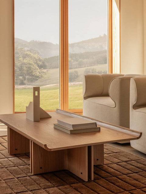 Audo Copenhagen Conrad Lounge Table, natural oak Conrad Lounge Table on a Tile Rug, paired with Eave Seamline Lounge Chairs overlooking a scenic landscape