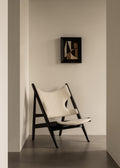 Modern Knitting Lounge Chair upholstered in light fabric with sculptural black frame, placed against a neutral wall.