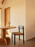 Audo Copenhagen Mauro Dining Chair, black oak Mauro Dining Chair with a paper cord seat beside a Puffin Dining Table and Admiral Portable Table Lamp