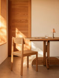 Audo Copenhagen Puffin Dining Table, Round, solid oak Puffin Dining Table and Mauro Dining Chair in a sunlit interior with an Admiral Portable Table Lamp