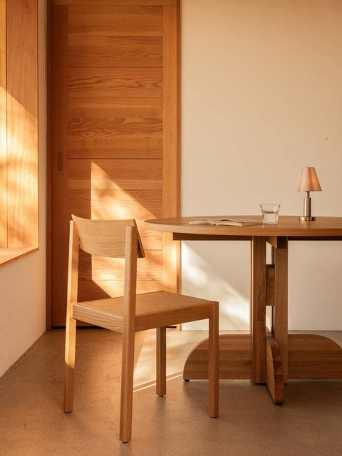 Audo Copenhagen Puffin Dining Table, Round, solid oak Puffin Dining Table and Mauro Dining Chair in a sunlit interior with an Admiral Portable Table Lamp