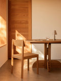 Audo Copenhagen Admiral Portable Lamp on a wooden Puffin Dining Table beside a Mauro Dining Chair in a warm, sunlit room