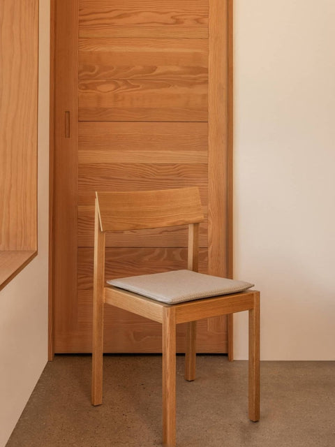 Audo Copenhagen Mauro Dining Chair Seat Cushion in light textile on a wooden Mauro Dining Chair against a warm timber door