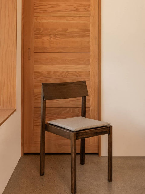 Audo Copenhagen Mauro Seat Cushion, dark wood Mauro Dining Chair with a light grey Mauro Dining Chair Seat Cushion in a minimalist room