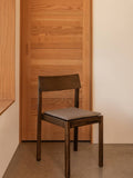 Audo Copenhagen Mauro Dining Chair, dark stained oak Mauro Dining Chair featuring a striped seat cushion, set against a light wood panelled sliding door