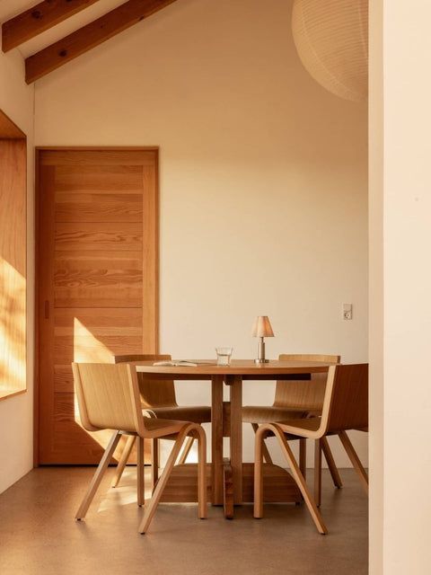 Audo Copenhagen Puffin Dining Table in oak with Ready Dining Chairs and an Admiral Portable Table Lamp in a warm minimalist setting