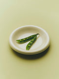 HAY Barro Bowls, Off-White, glazed terracotta serving bowl, close-up from above holding two pea pods on a pale green surface