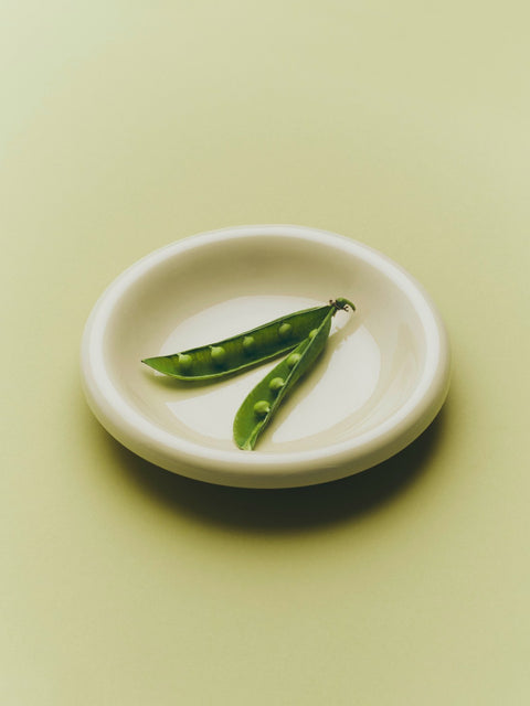 HAY Barro Bowls, Off-White, glazed terracotta serving bowl, close-up from above holding two pea pods on a pale green surface