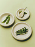 HAY Barro Plates, Ø24, Off-White, glazed terracotta plates, overhead with pea pods, a halved pear and green beans on pale green