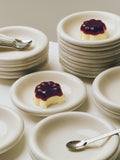 HAY Barro Bowls, Off-White, glazed terracotta bowls and plates, stacked beside a berry topped dessert with forks and a spoon