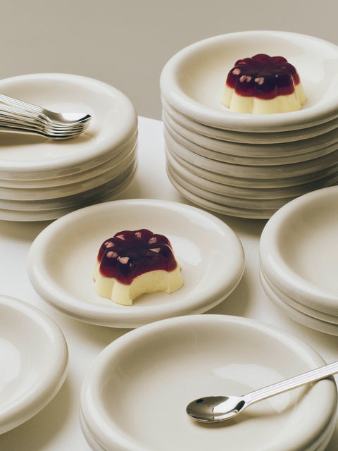 HAY Barro Bowls, Off-White, glazed terracotta bowls and plates, stacked beside a berry topped dessert with forks and a spoon