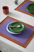 HAY Barro Plates, Green, glazed portuguese terracotta plates, overhead on a purple placemat with a light blue bowl, blue spoon and terracotta mug