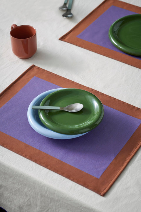 HAY Barro Plates, Green, glazed portuguese terracotta plates, overhead on a purple placemat with a light blue bowl, blue spoon and terracotta mug
