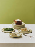 HAY Barro Plates, Pistachio, glazed portuguese terracotta plates, a stack topped with bread beside plates of green beans and dips, olive backdrop
