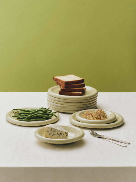 HAY Barro Plates, Pistachio, glazed portuguese terracotta plates, a stack topped with bread beside plates of green beans and dips, olive backdrop