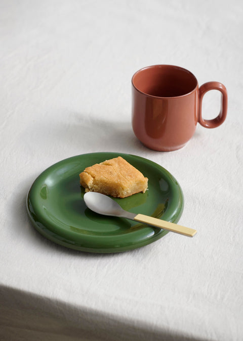 HAY Barro Cups, Natural, terracotta cups, one cup on white linen beside a green glazed plate of cake and yellow handled cutlery