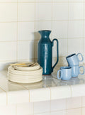 HAY Barro Cups, Light Blue, terracotta cups, two pale blue cups beside a teal jug and stacked off-white plates on a tiled ledge