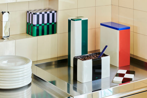 HAY Tin Container, Small, Dark Blue and Lavender, lidded tinplate storage tin, stacked on a green tin on a tiled ledge above a steel counter