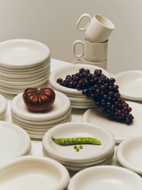 HAY Barro Bowls, Off-White, glazed terracotta bowls and plates, stacked in tall piles with grapes, a tomato and a pea pod