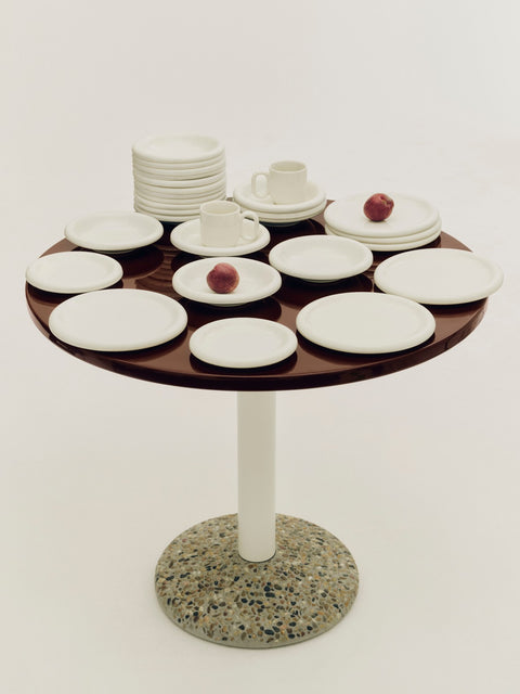 HAY Barro Plates, Ø24, Off-White, glazed terracotta tableware, filling a round dark red table with a terrazzo base and cream tube