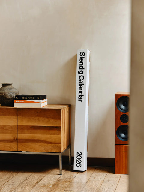 Tall white box packaging for the 2026 Stendig Calendar standing beside a console