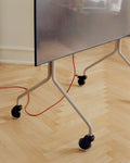 Pedestal Blade Wheels in Black, fitted to the legs of a pale TV stand, seen close up on a herringbone floor