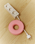 Pedestal Cable Bagel in Bubble Gum, silicone ring winding a white cable, on a wooden table beside a power bar