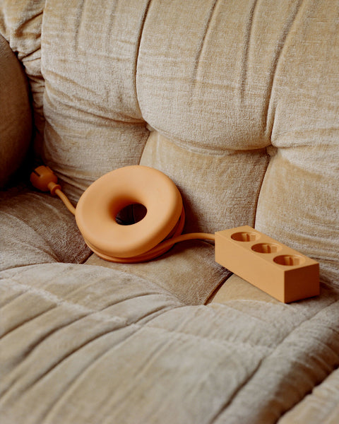 Pedestal Cable Bagel in Apricot, silicone ring with a cable wound through it, resting on a cream corduroy sofa