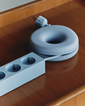 Pedestal Cable Bagel in Powder Blue, silicone ring with its cable and plug, on a wooden table beside a power bar