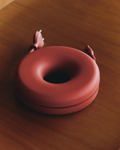Pedestal Cable Bagel in Burnin' Red, silicone cable ring seen close up on a dark wooden table