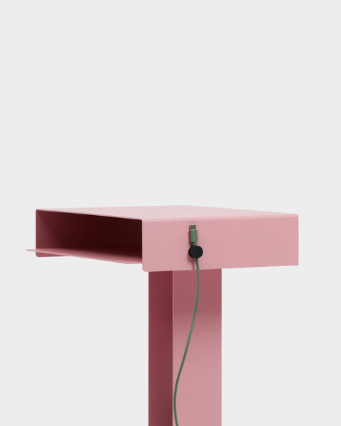 Pedestal Cable Clips in Charcoal, magnetic silicone cable clip, holding a cable against the edge of a pink desk