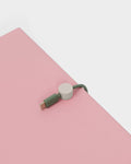 Pedestal Cable Clips in Oat, magnetic silicone cable clip, holding a cable on a pink surface seen close up