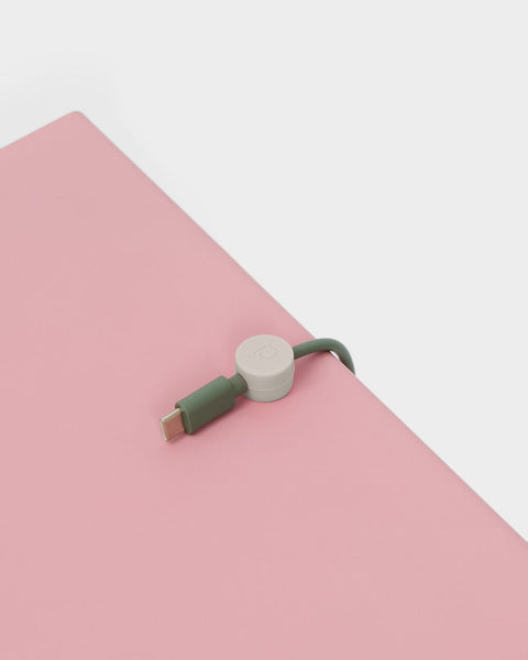 Pedestal Cable Clips in Oat, magnetic silicone cable clip, holding a cable on a pink surface seen close up