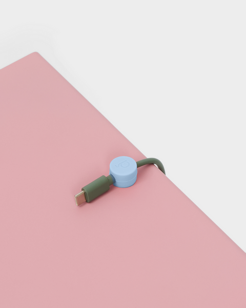 Pedestal Cable Clips in Powder Blue, magnetic silicone cable clip, holding a cable on a pink surface seen close up