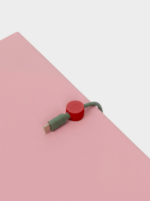 Pedestal Cable Clips in Burnin' Red, magnetic silicone cable clip, holding a cable on a pink surface seen close up