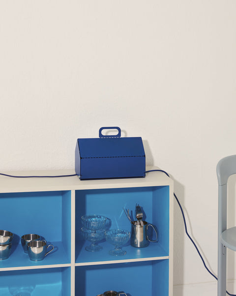 Pedestal Cable House in Ultra Marine, closed on top of a blue cube shelf holding glassware, cable running down
