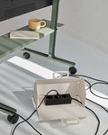 Pedestal Cable House in Pearl, open with a power bar inside, on the floor beneath a green desk with cables running out