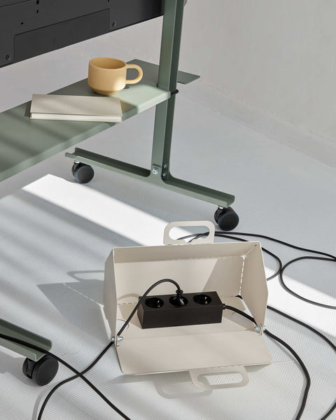 Pedestal Cable House in Pearl, open with a power bar inside, on the floor beneath a green desk with cables running out