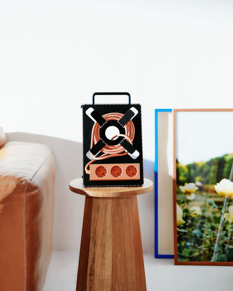Pedestal Cable Stand in Charcoal, holding a power bar and coiled cable upright on a round wooden side table