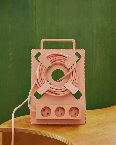 Pedestal Cable Stand in Dusty Rose, holding a coiled cable and power bar on a wooden table against a green wall