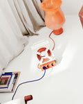 Pedestal Cable Stand in Pearl, lying on a white bed with a coiled cable, seen from above beside a terracotta vase