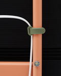 Pedestal Cable Tie in Mossy Green, soft silicone cable tie, holding a cable against the leg of an Apricot TV stand