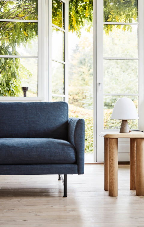 Close up of Fredericia Calmo 3 Seater arm in blue next to a solid oak side table by a bright window