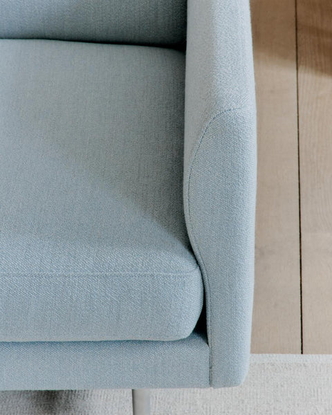Detail of Calmo sofa arm and seat in light blue upholstery with slim matte chrome leg