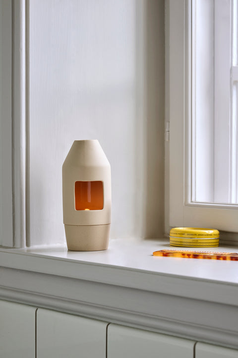 HAY Chim Chim Scent Diffuser, Light Beige, ceramic tealight scent diffuser, glowing on a white windowsill beside yellow incense coils
