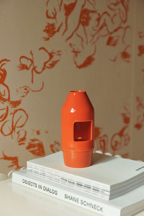 HAY Chim Chim Scent Diffuser, Red, glossy ceramic tealight scent diffuser, on a stack of white books by a hand drawn mural wall