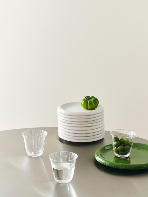 HAY Barro Plates, Green, glazed portuguese terracotta plates, a green plate and glasses beside a stack of plates topped with a green tomato
